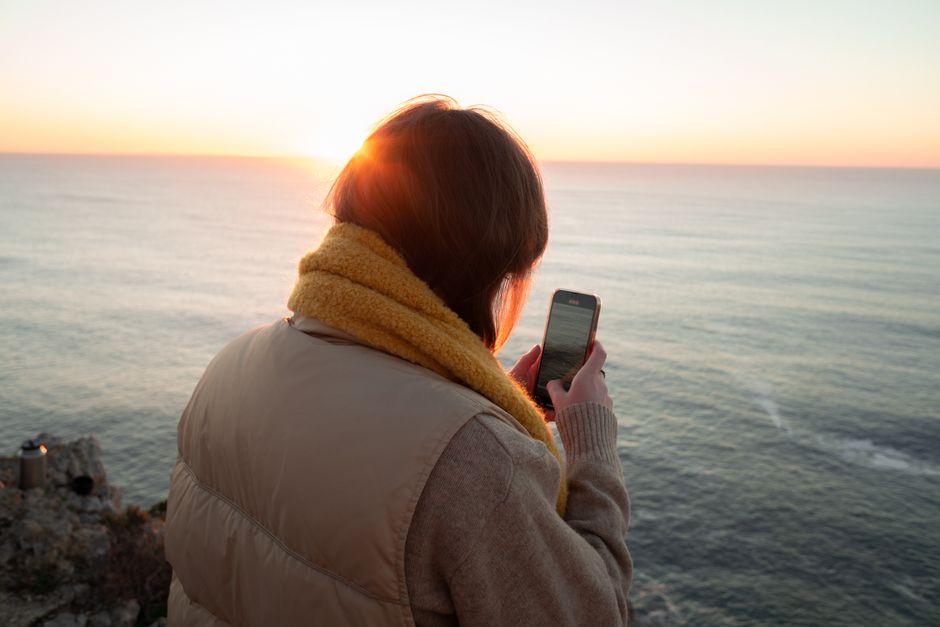 Woman using smartphone at seaside during sunset, enjoying the peaceful view.