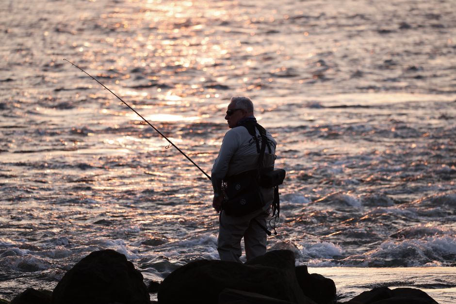 Silhouette of a man fishing by the ocean during sunset. Peaceful evening moment on the rocky shore.