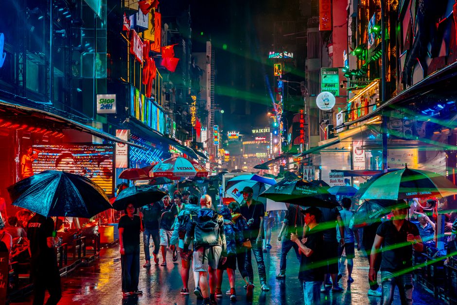 Colorful neon-lit street bustling with people under umbrellas at night.