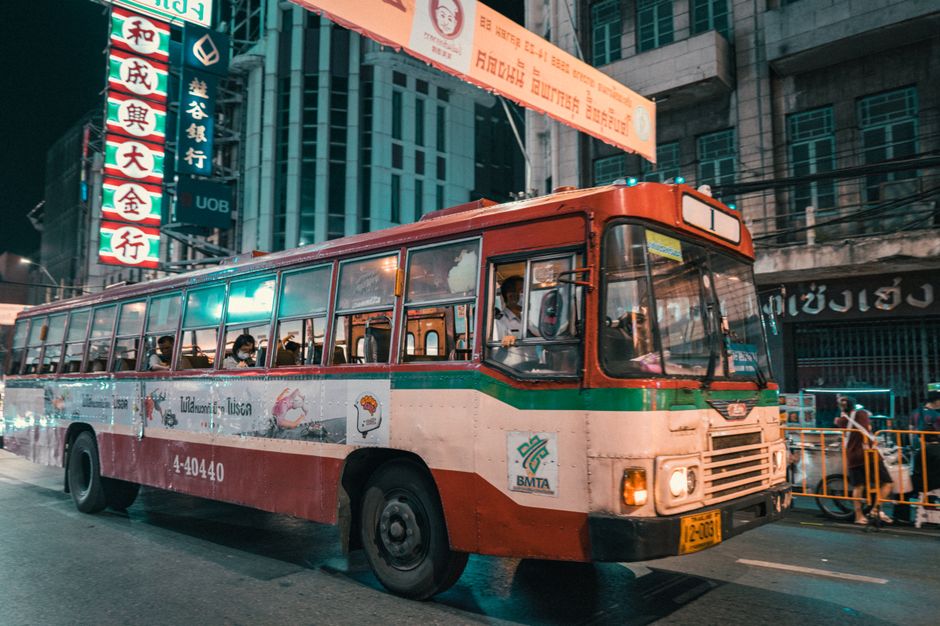 A vintage bus navigates the neon-lit streets of Bangkok at night, showcasing vibrant city life.
