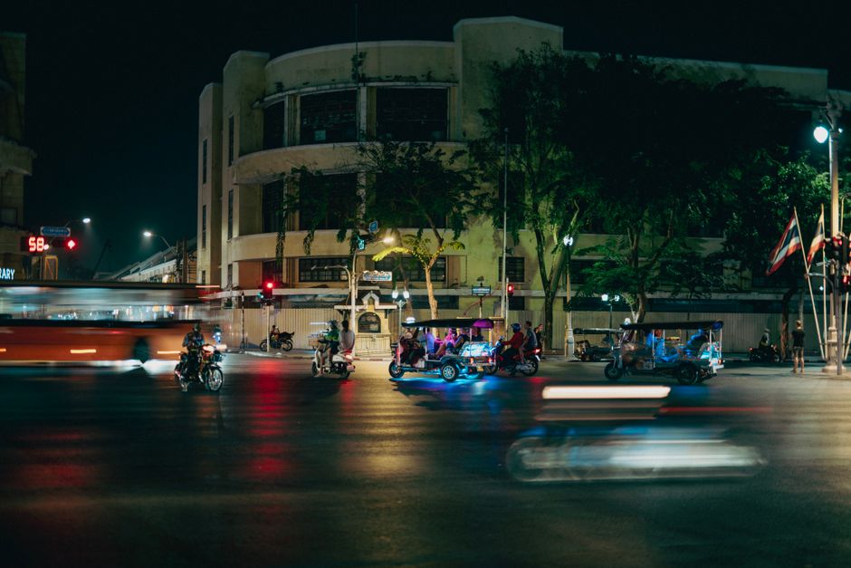 Vibrant city nightlife featuring tuk-tuks and motorcycles on a busy street corner with blurred motion.