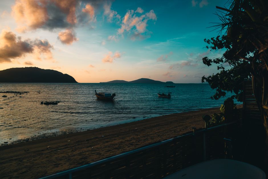 Tranquil sandy beach with boats and islands at sunset in Phuket, Thailand.