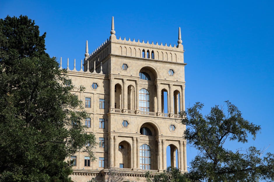 An ornate historical building in Baku against a clear blue sky, framed by lush green trees.