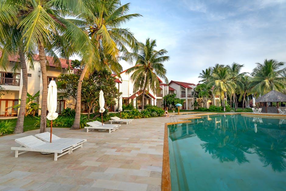 Relaxing poolside view with coconut trees and villas at a tropical resort.