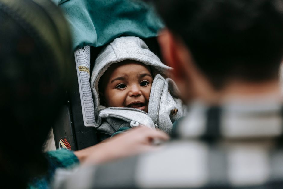 Back view of crop unrecognizable parents caressing cute African American baby in warm clothes sitting in stroller on street