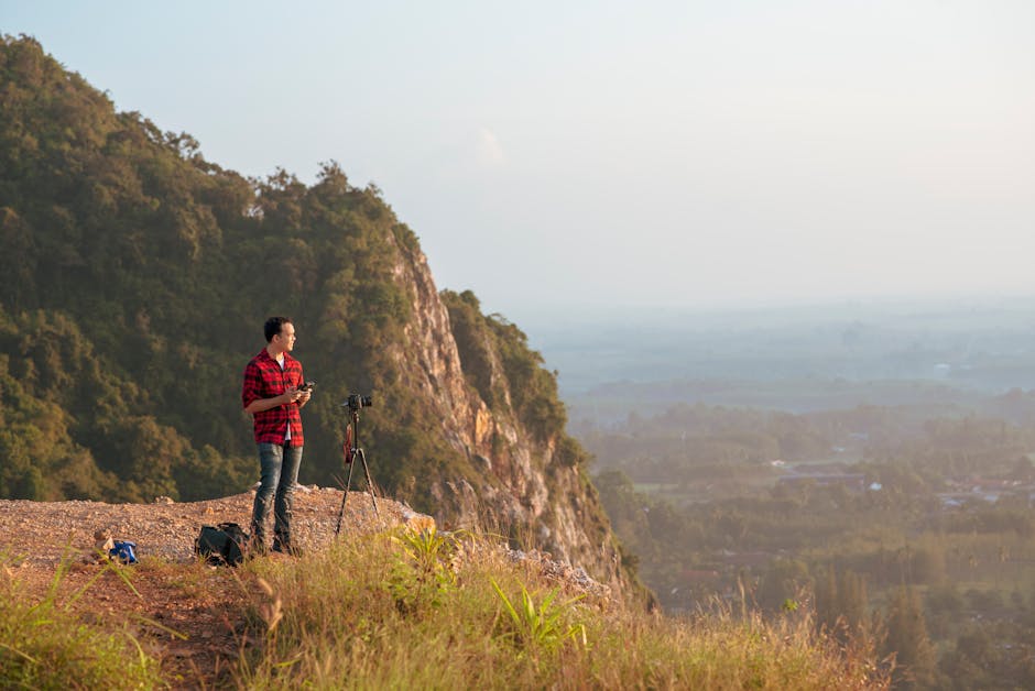 Photographer with tripod atop a mountain cliff capturing breathtaking landscape views.