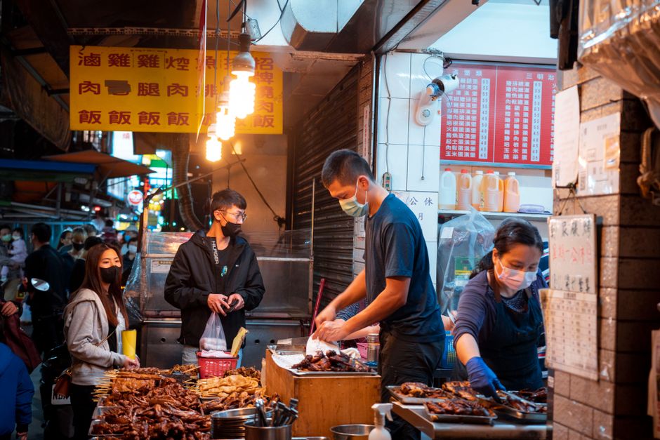People buying grilled meats at an Asian night market food stall. Bustling evening atmosphere.