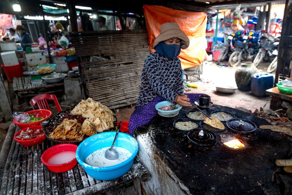Masked vendor cooking traditional Asian street food outdoors in local market.