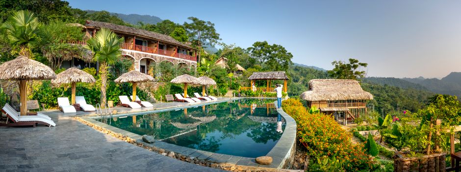 Amazing scenery of small hotel and swimming pool with deckchairs and umbrellas located on top of green hill in tropical resort