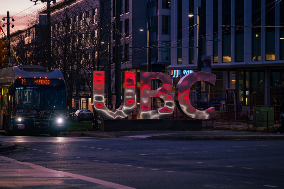 Evening scene of UBC sign illuminated with city bus at University Endowment Lands in Vancouver, BC.