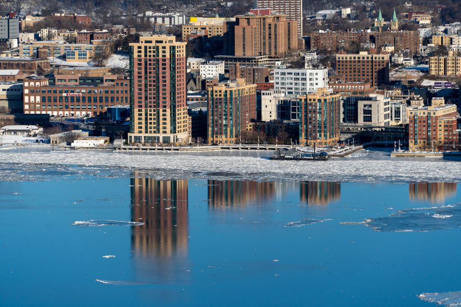 A scenic coastal cityscape with buildings reflecting on icy water during winter.