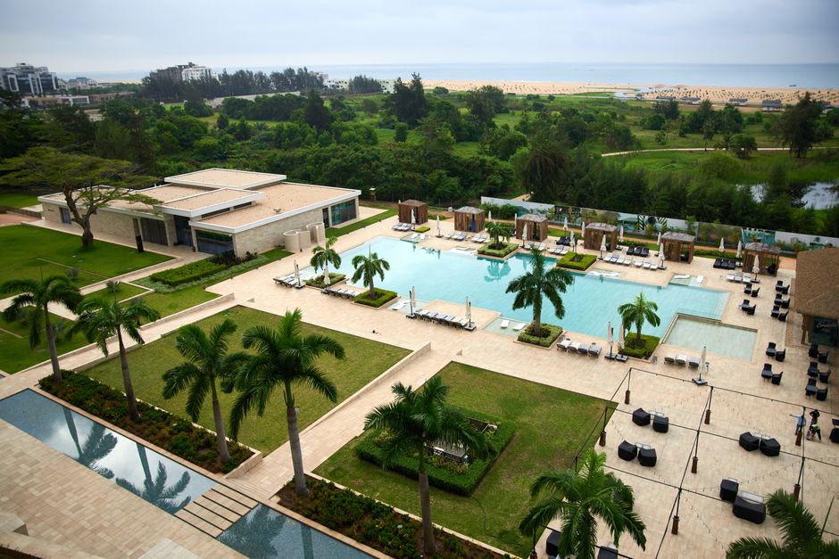 Aerial view of a luxury resort pool area with lush greenery and beach access.