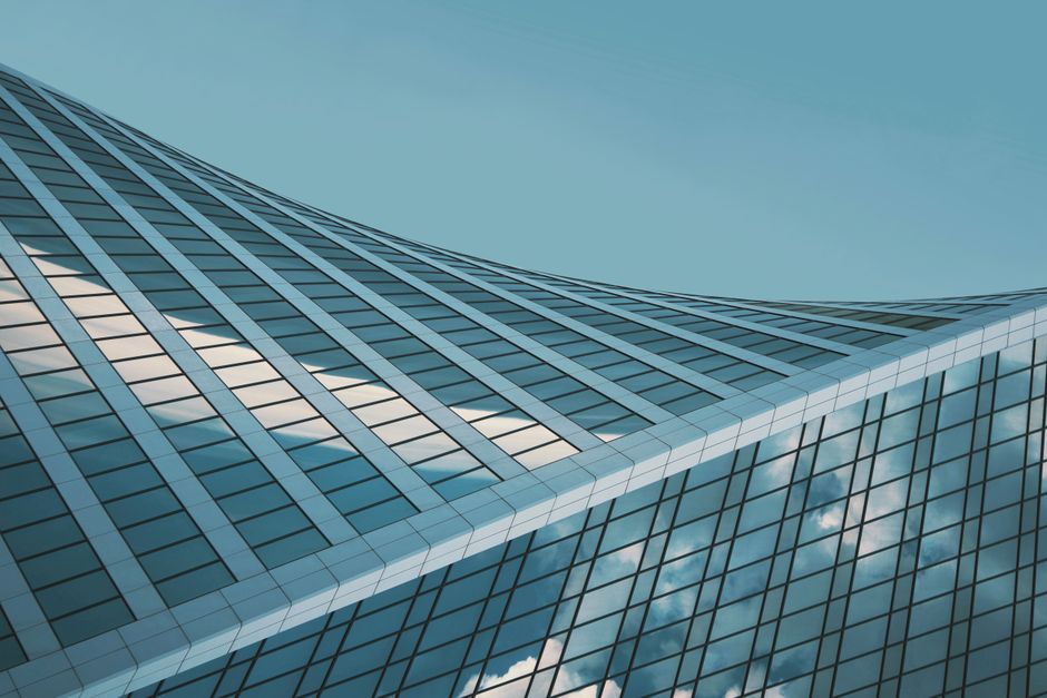 Distinctive curved glass building reflecting clouds in a clear sky.