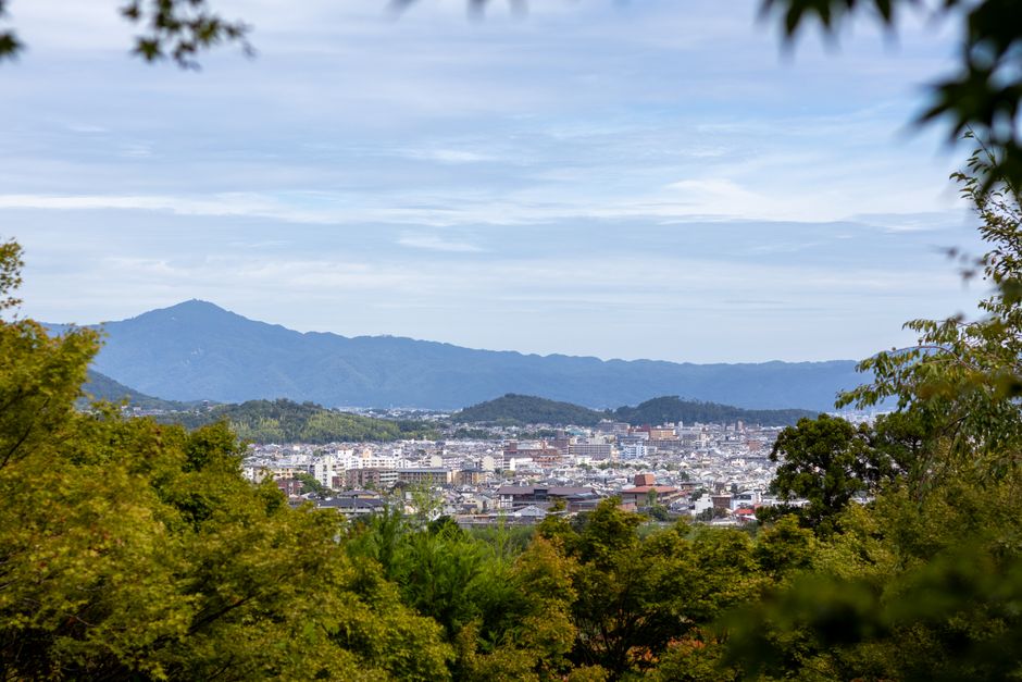 A scenic view of Kyoto with lush greenery and mountain backdrop under a clear sky.