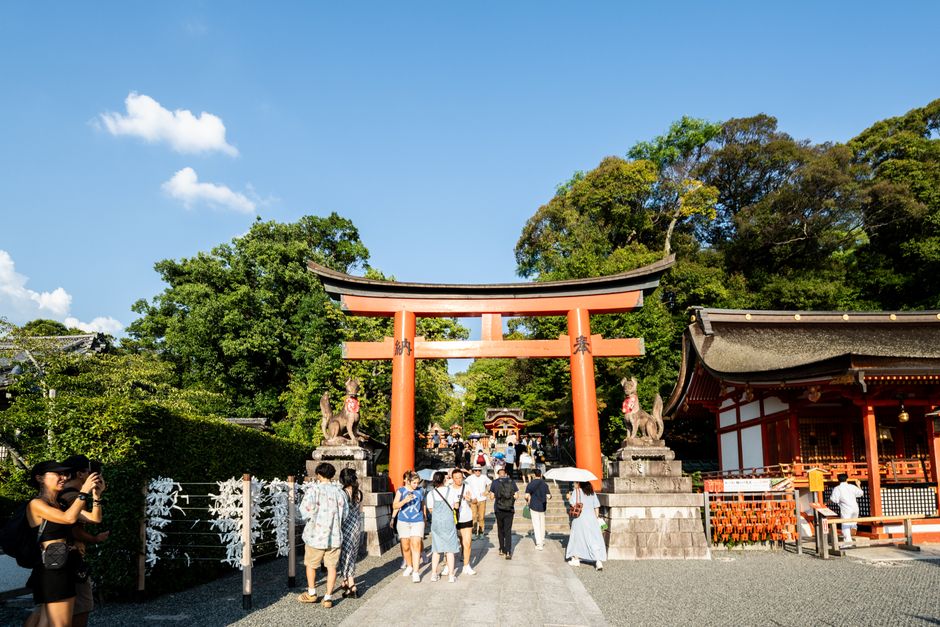 Crowds explore the iconic Fushimi Inari Taisha shrine in Kyoto on a sunny day.