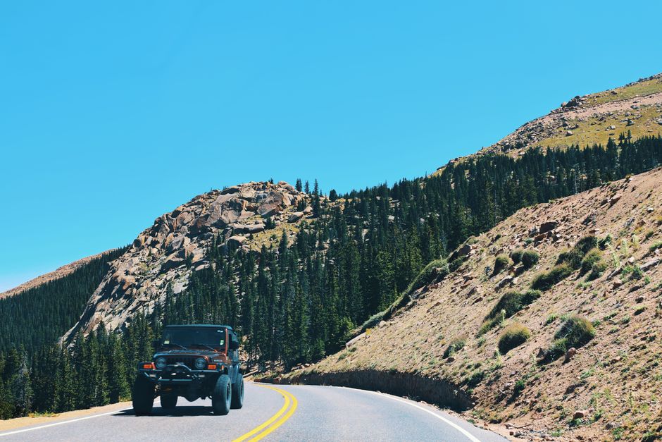 A vehicle navigates a winding road through the Rocky Mountains under a clear blue sky.