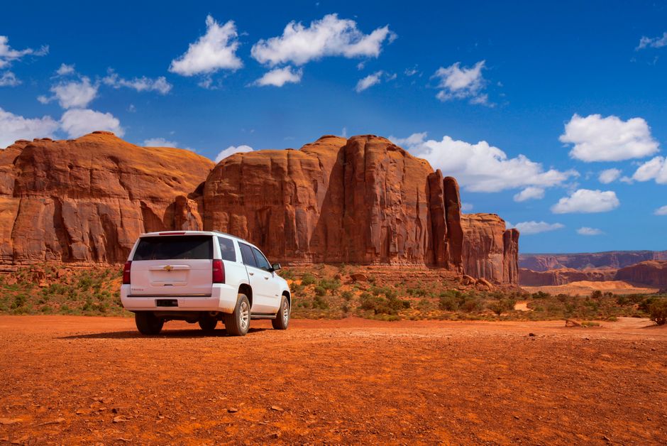 A white SUV parked amidst the breathtaking red rock formations of Monument Valley under a clear blue sky.