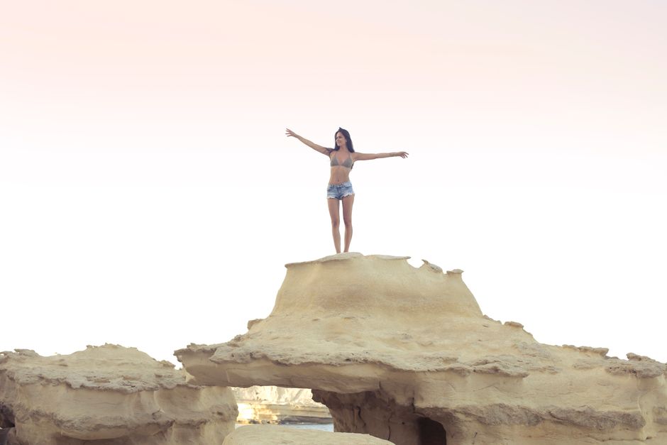 Young woman enjoying a sunny day on a rock formation in Mgarr, Malta.