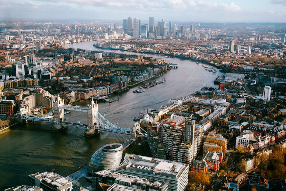 Aerial view of London's Tower Bridge and cityscape along the River Thames, showcasing urban architecture.