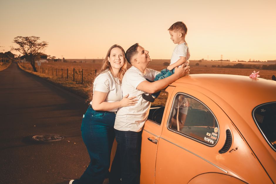 A joyful family enjoying time together with a classic car during a warm sunset on a rural road.