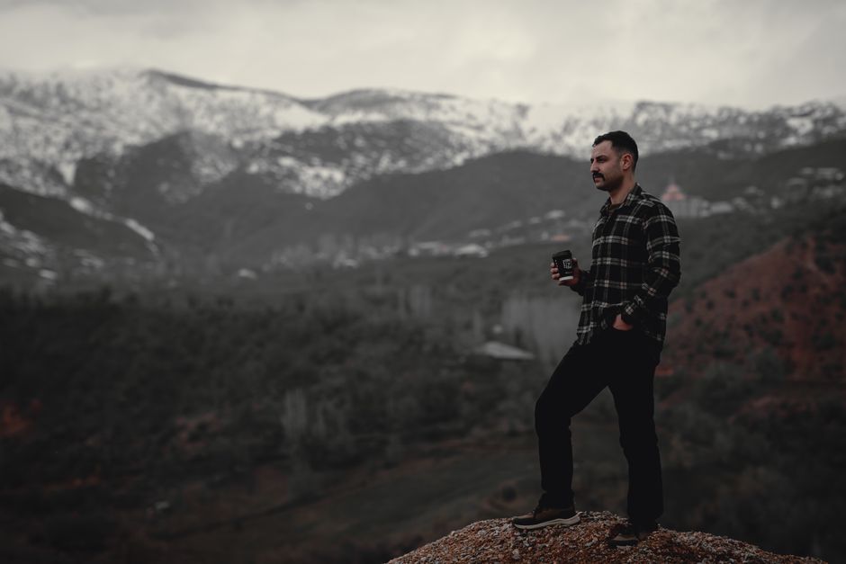 A man stands with a cup, enjoying a serene mountain view, representing adventure and tranquility.