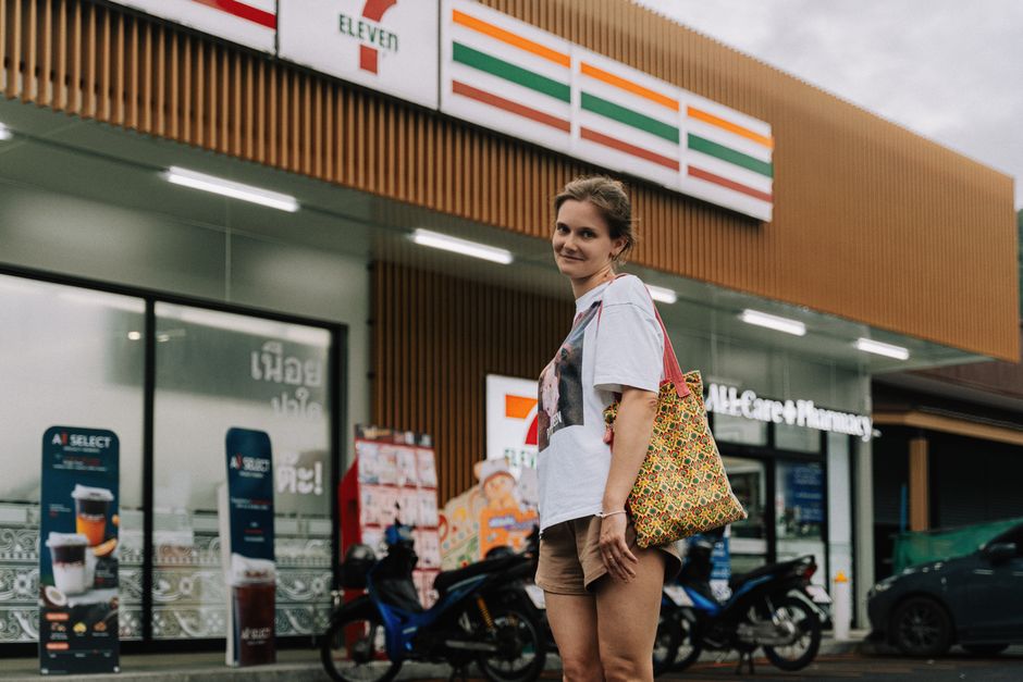 A woman standing in front of a 7-Eleven store in Phuket, Thailand, with a casual pose.