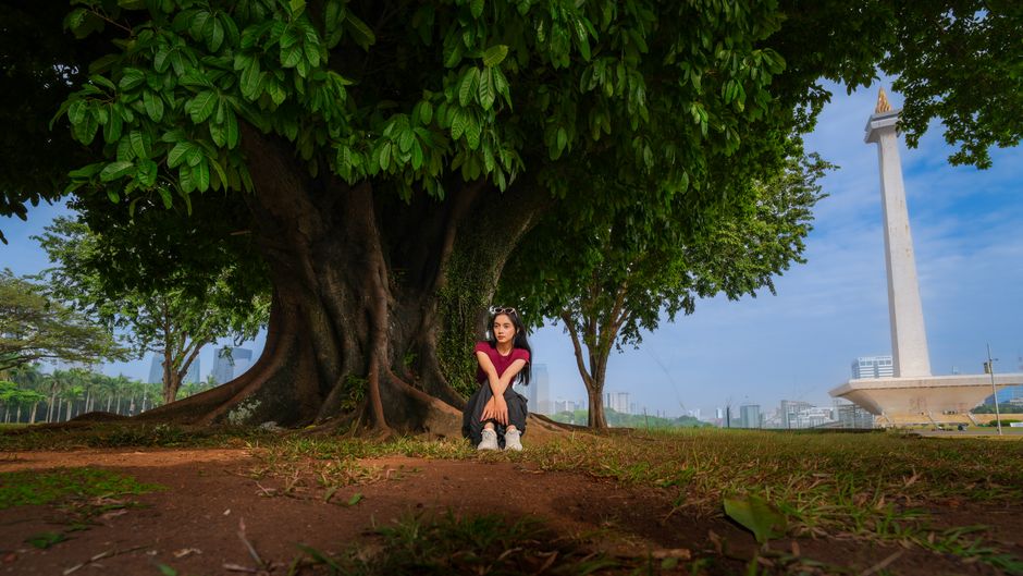 Woman sitting under tree near the National Monument in Jakarta.