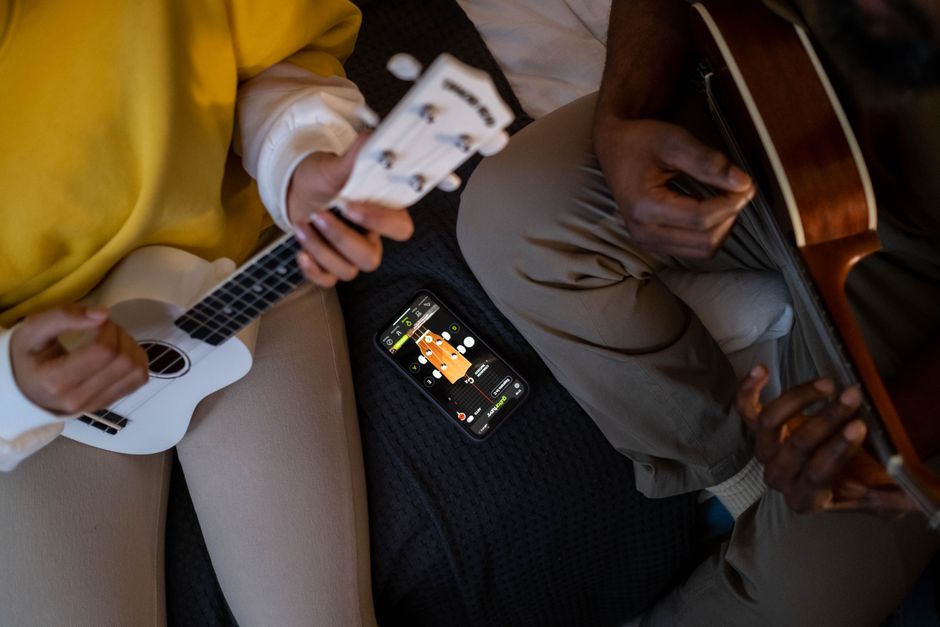 Top view of two people playing guitars using a smartphone app to learn chords.