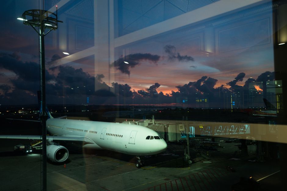 Through glass modern white plane connected to airport terminal with airbridge and ready for boarding against spectacular cloudy purple sky in late evening