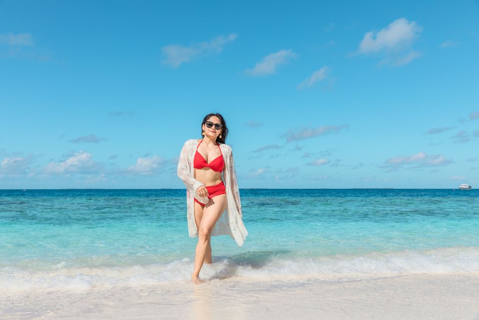 A woman in a red bikini walks along a pristine tropical beach with clear blue water.