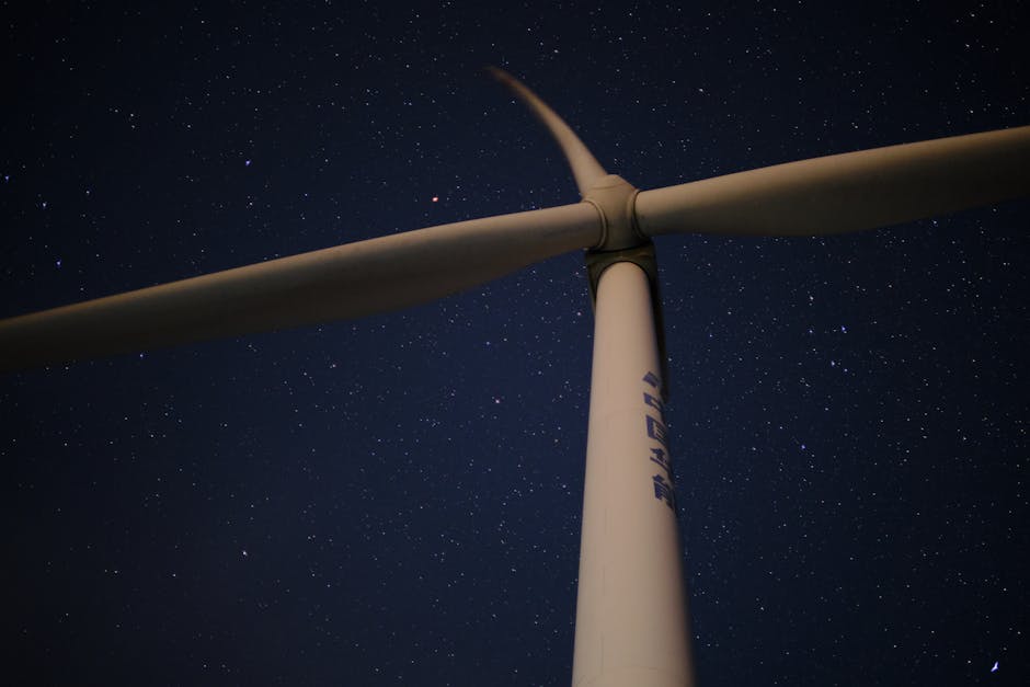 A low angle view of a wind turbine against a clear, star-filled night sky, symbolizing renewable energy.